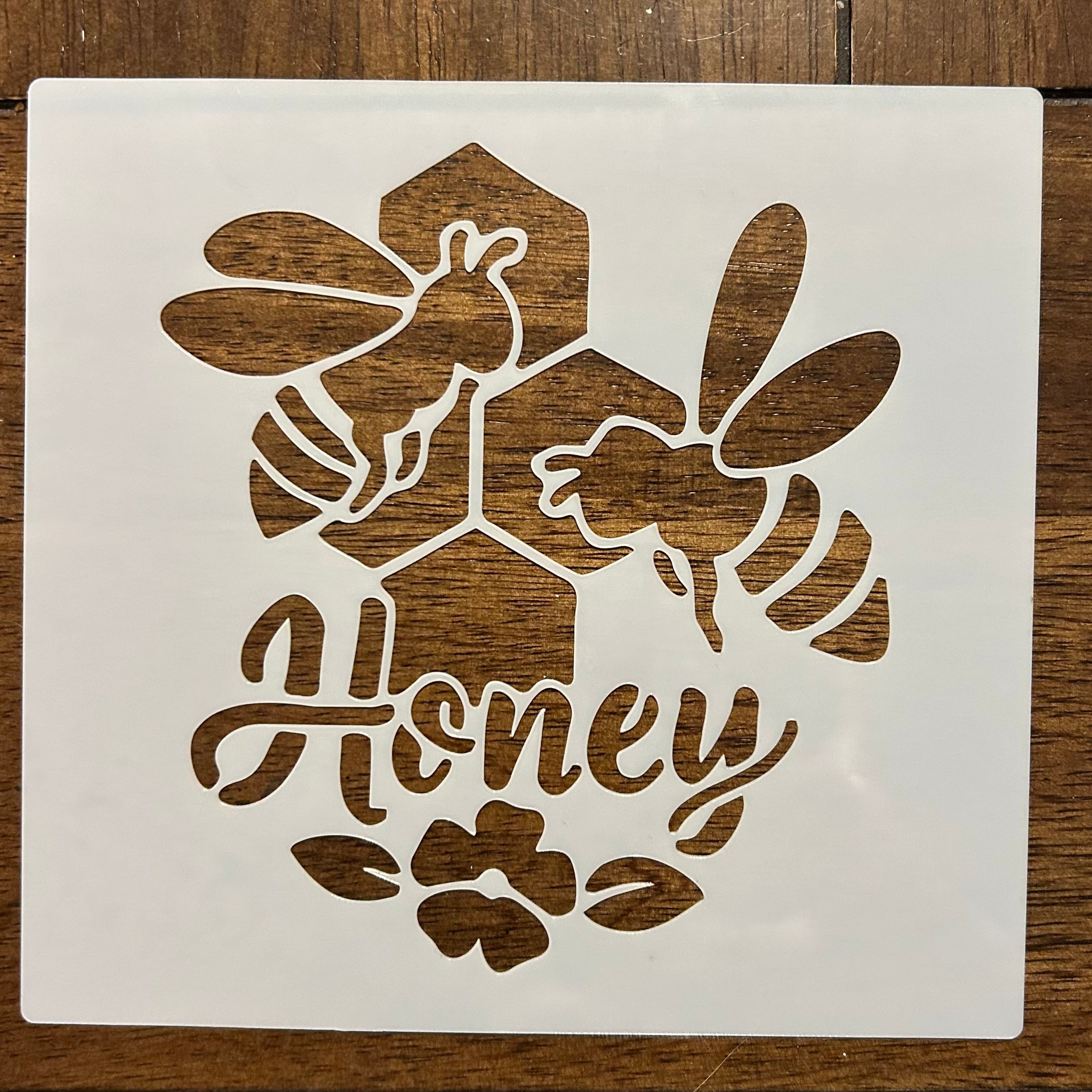 Decorative stencils with bee designs and 'All Honey' text on a wooden surface