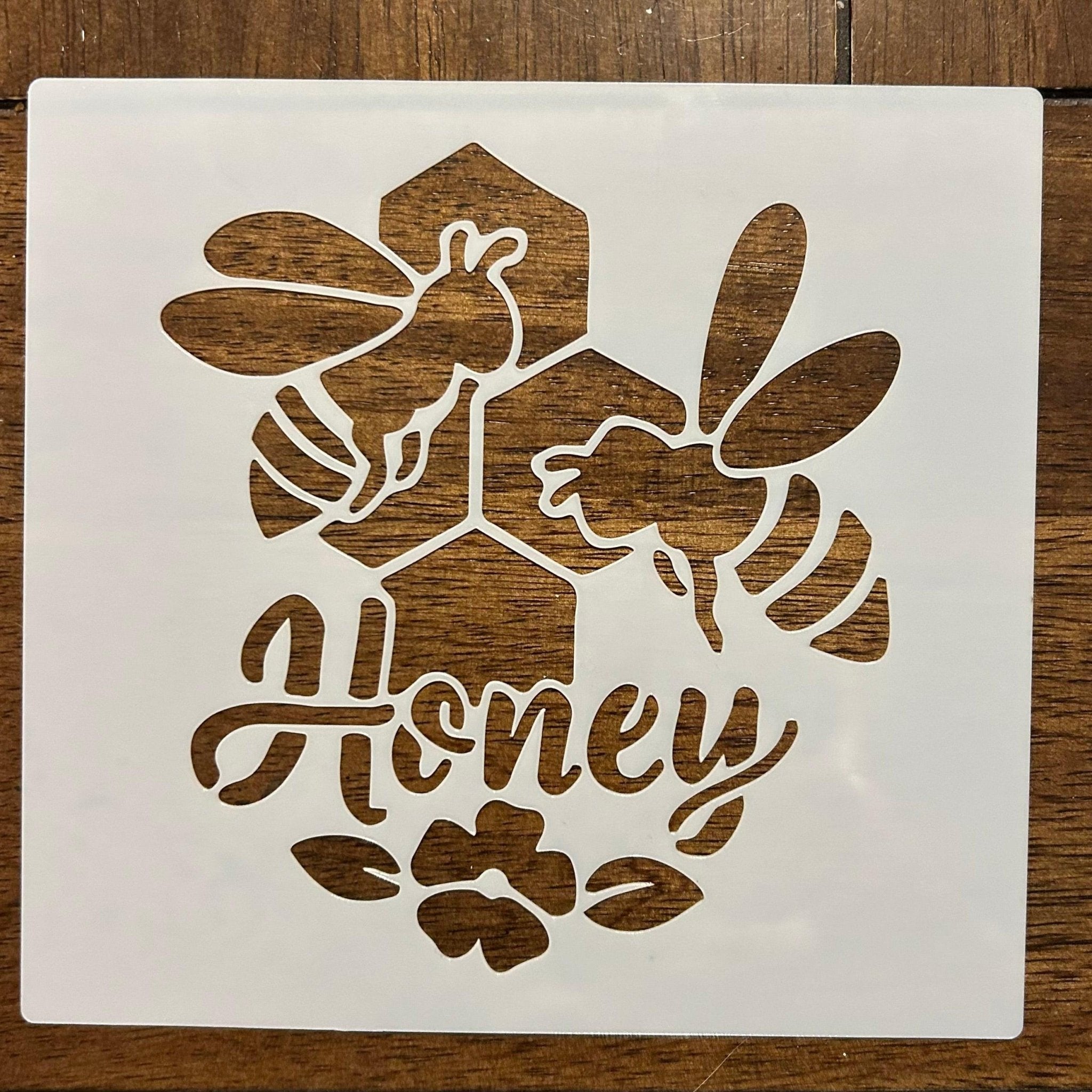 Decorative stencils with bee designs and 'All Honey' text on a wooden surface